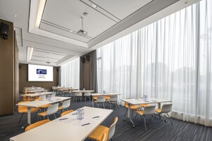 A conference room with tables, chairs, a projector screen, and large windows with curtains.