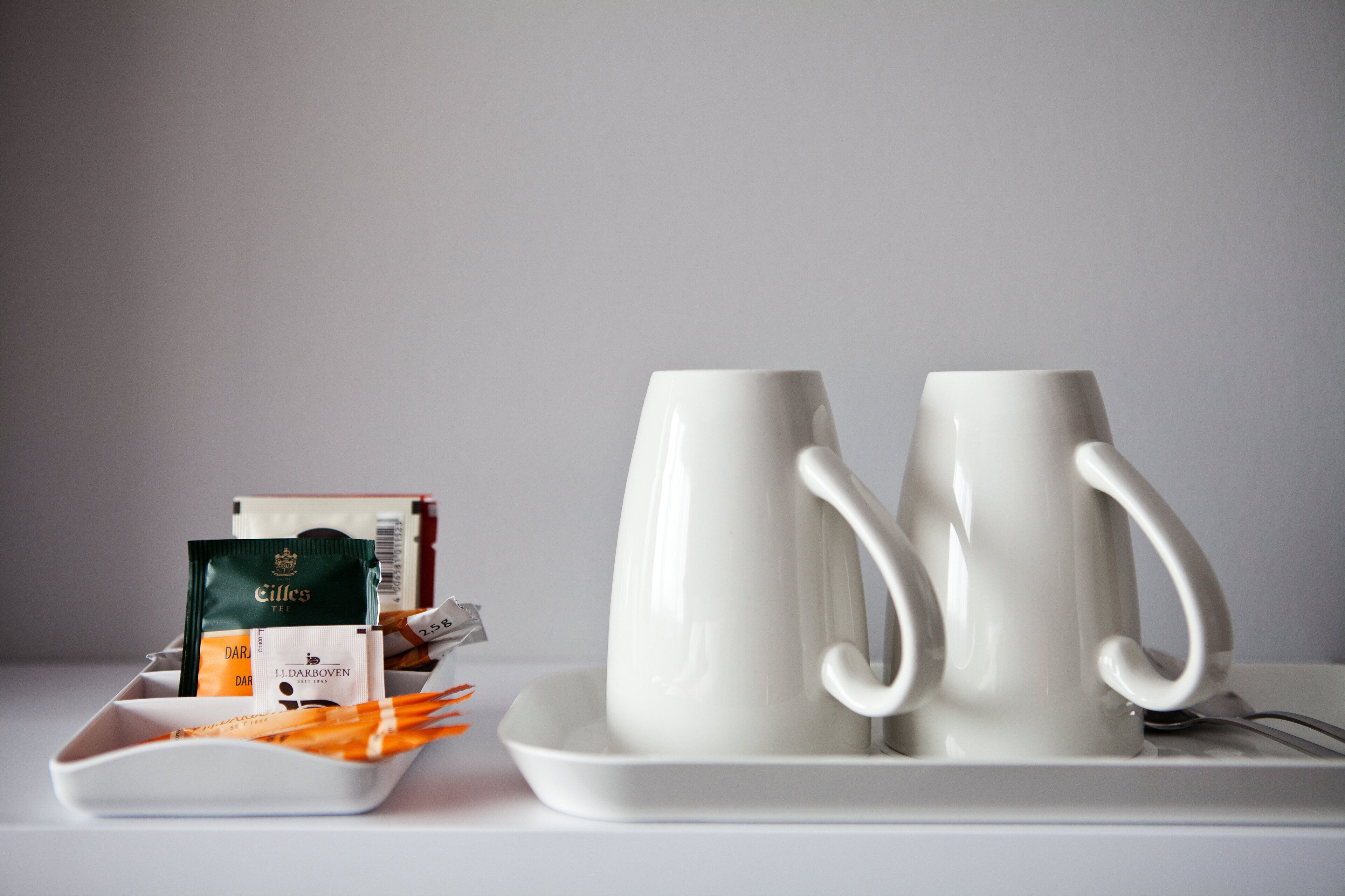 Two white ceramic mugs on a white tray with a plate of orange straws and tea packets.