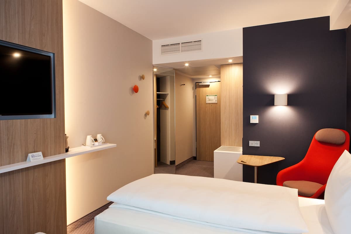 Une chambre d’hôtel moderne avec un lit, une télévision, un fauteuil rouge et une petite table.