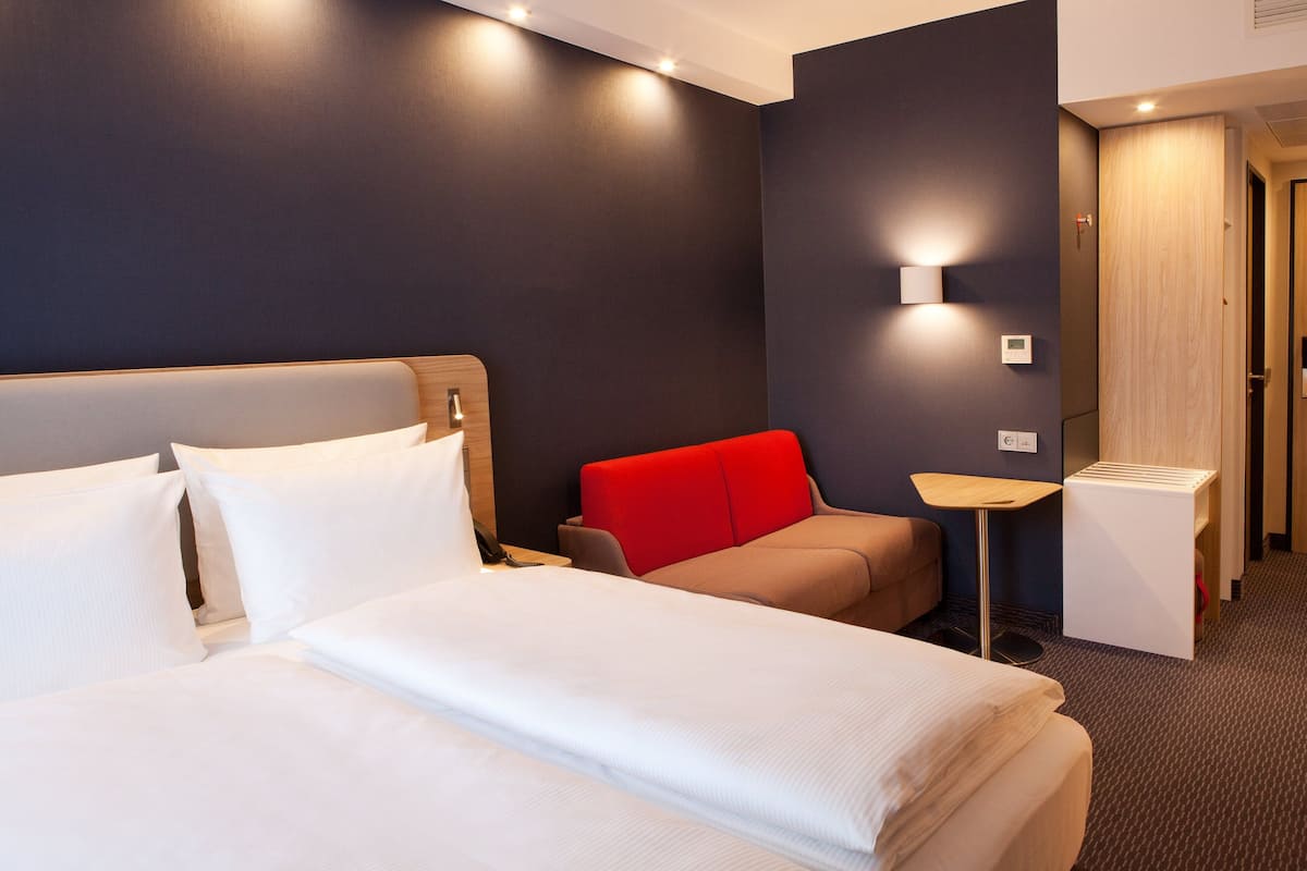 Une chambre d’hôtel avec deux lits, une chaise rouge, une petite table et une armoire en bois.