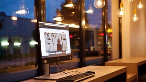 A computer monitor on a desk with a keyboard, a mouse, and a window with a view of city lights. - Holiday Inn Express Offenburg by IHG (Offenburg)