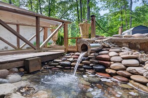 Une structure en bois agrémentée d’un élément aquatique, entourée de rochers et de verdure.