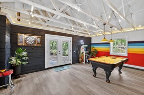 Une pièce équipée d’une table de billard, de cibles de fléchettes et d’une porte donnant sur un espace extérieur.