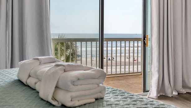 Ett hotellrum med en säng, utsikt över stranden och en balkong med ett räcke.