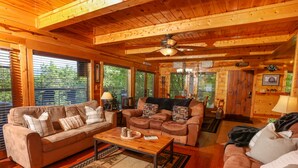 A cozy log cabin interior with a wooden ceiling, two sofas, a coffee table, and a ceiling fan.