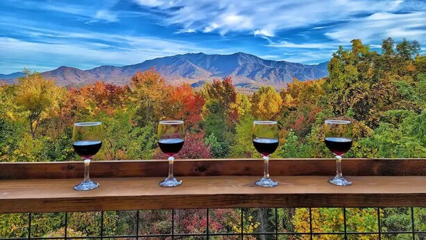 A wooden balcony with four wine glasses and a scenic mountain view.