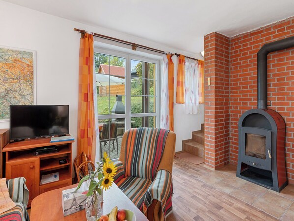 A living room with a television, a sofa, a table with a vase and fruit, and a fireplace. - Vacation home Zásada by Interhome (Zasada)