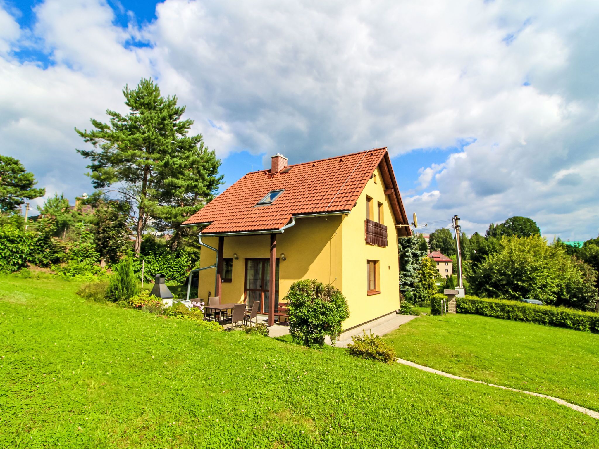 Une maison jaune avec un toit rouge, entourée d’herbe verte et d’arbres.