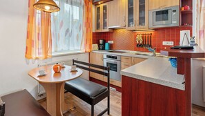 Een compacte keuken met houten kastjes, een magnetron en een kleine eethoek met een bankje en tafel.