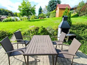 An outdoor patio with a wooden table and wicker chairs, a barbecue grill, and a small wooden building in the background. - Vacation home Zásada by Interhome (Zasada)