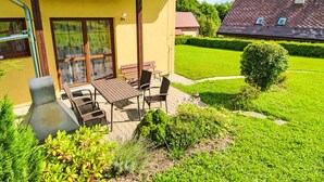 Een geel gebouw met pannendak, een terras met tafel en stoelen, en een verzorgd gazon.