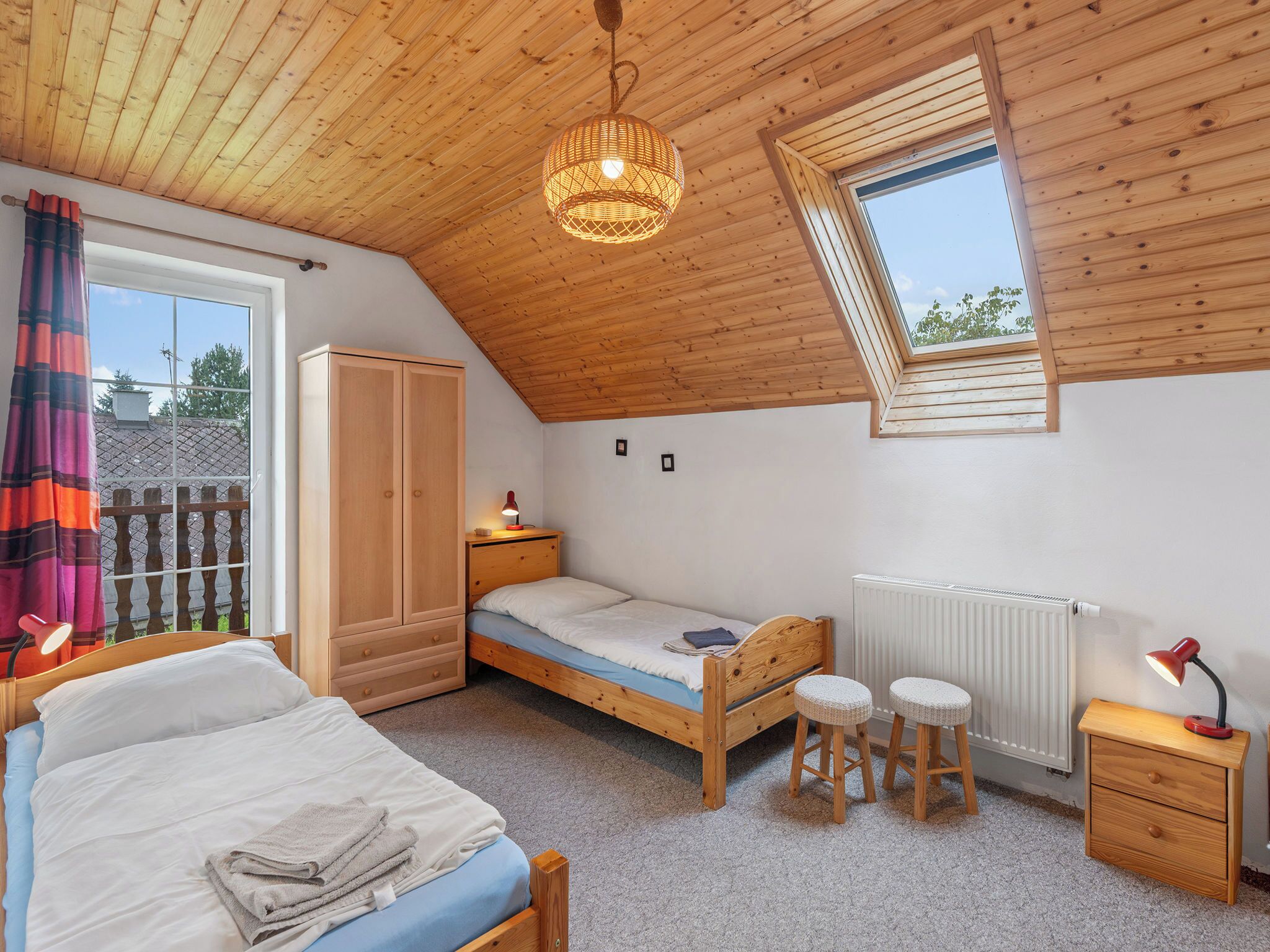 Une chambre avec un plafond en pente, un puits de lumière, un lit, une armoire, une table de chevet et un radiateur.