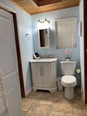 Une salle de bain équipée d’un meuble-lavabo, d’un évier, d’un miroir, de toilettes et d’une fenêtre avec des stores.