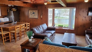 Een gezellig houten vakantiehuisje met een eethoek, een leren bank en uitzicht op een meer door grote ramen.