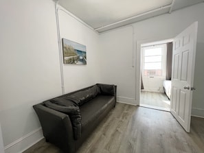 A room with a dark leather sofa, a white door, and a window with curtains. - Modern Beachfront Suite 206 (Ocean City)