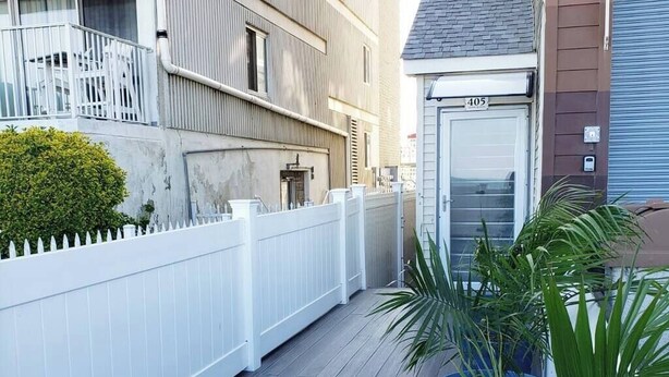 A residential building with a white picket fence, a door labeled '405', and potted plants on the porch. - Modern Beachfront Suite 206 (Ocean City)