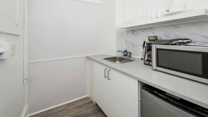 A compact kitchen with white cabinets, a stainless steel sink, a microwave, and a dishwasher. - Modern Beachfront Suite 206 (Ocean City)