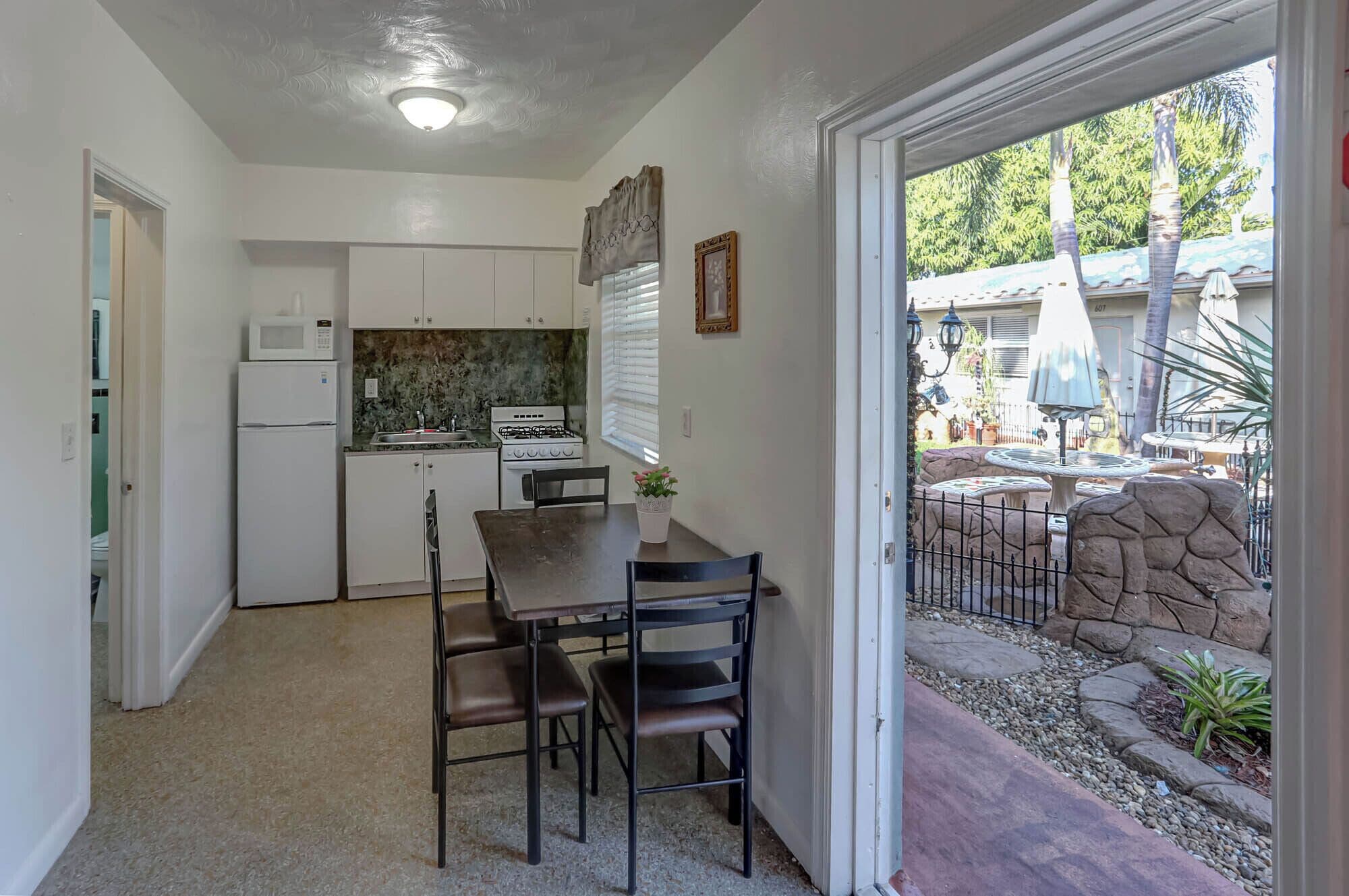 A compact kitchen with white cabinets, a refrigerator, a stove, and a dining table with four chairs.