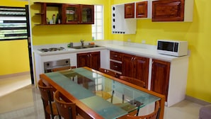 Een keuken met een glazen eettafel, houten keukenkastjes, een magnetron en een fornuis.