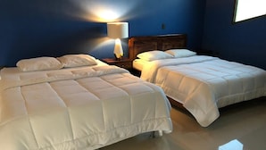 Een hotelkamer met twee bedden, een nachtkastje met een lamp, en een raam dat natuurlijk licht biedt.