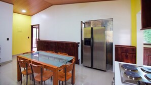 Een moderne keuken met een eettafel met glazen blad, houten stoelen, een roestvrijstalen koelkast en een gasfornuis.