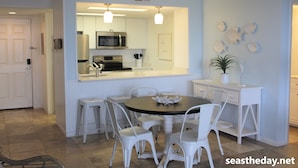 A modern kitchen with white cabinetry, a central island, and a dining area with white chairs. - Ocean view, 2BR, 2BA Condo, St. Regis #3213, Topsail, NC (North Topsail Beach)