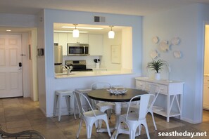 A modern kitchen with white cabinetry, a central island, and a dining area with white chairs.