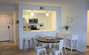 A modern kitchen with white cabinetry, a central island, and a dining area with white chairs. - Ocean view, 2BR, 2BA Condo, St. Regis #3213, Topsail, NC (North Topsail Beach)