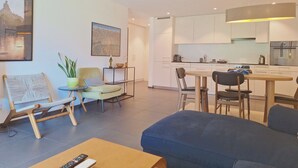 A modern living room with a sofa, a dining table with chairs, a small side table with a plant, and a framed picture on the wall.