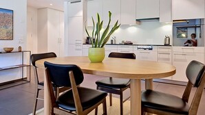 A modern kitchen with white cabinets, a round dining table with chairs, and a potted plant.