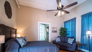 A bedroom with a large bed, a sofa, a ceiling fan, and a view of the outdoors.