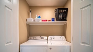 A laundry room with two washing machines and a shelf above them.
