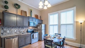 A modern kitchen with dark cabinets, a marble backsplash, and a dining area with a wooden table and chairs.