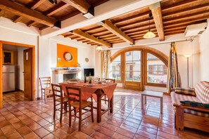 Zona pranzo con tavolo e sedie in legno, cucina con frigorifero e un angolo salotto accogliente con divano.