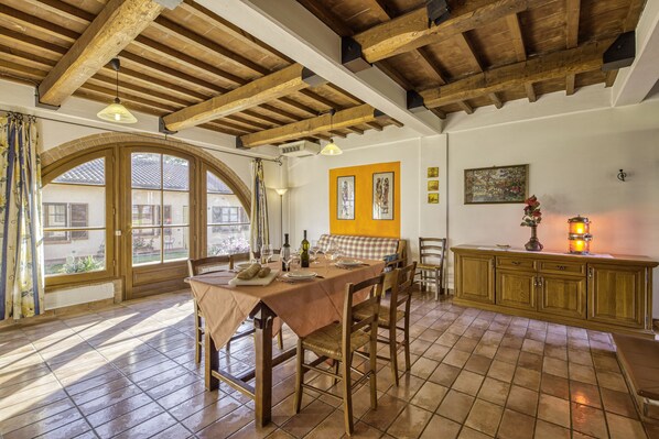 A dining area with a wooden table and chairs, a checkered bench, and a wooden cabinet with a candle. - Apartment Ginepro Shared Pool for 5 pax, Castiglione del Lago, Italy (Castiglione del Lago)