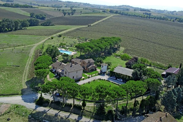 Vista aerea di una proprietà rurale con diversi edifici, una piscina e campi circostanti.
