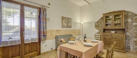 Un coin repas avec une table dressée pour quatre personnes, des chaises en bois, un mur en pierre et un buffet en bois doté de portes en verre.