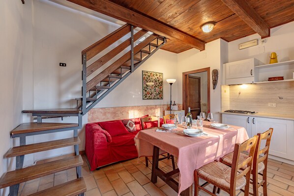 A dining area with a wooden staircase, a red sofa, and a table set for two. - Rosa Canina apt With Shared pool 4 pax, Castiglione del Lago, Italy (Castiglione del Lago)
