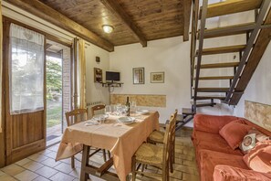 A dining area with a table set for four, a red sofa, and a wooden staircase. - Rosa Canina apt With Shared pool 4 pax, Castiglione del Lago, Italy (Castiglione del Lago)