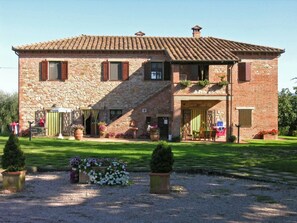 Traditional farmhouse with a central entrance, surrounded by a well-maintained lawn and potted plants.
