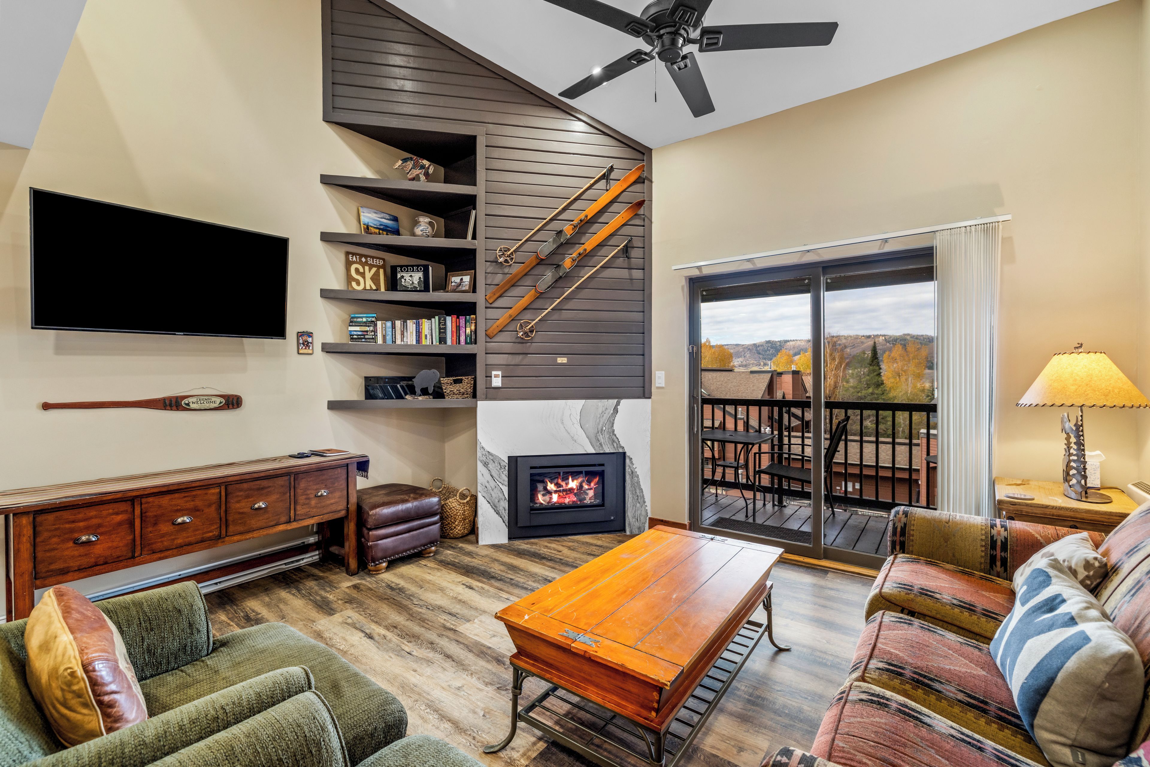A living room with a fireplace, a television, a bookshelf, and a view of the outdoors.
