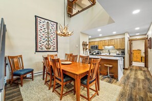 A dining area with a wooden table and chairs, a chandelier, and a large decorative tapestry on the wall.