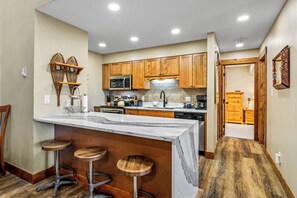 Cocina con armarios de madera, una isla de mármol con taburetes y vistas al comedor contiguo.
