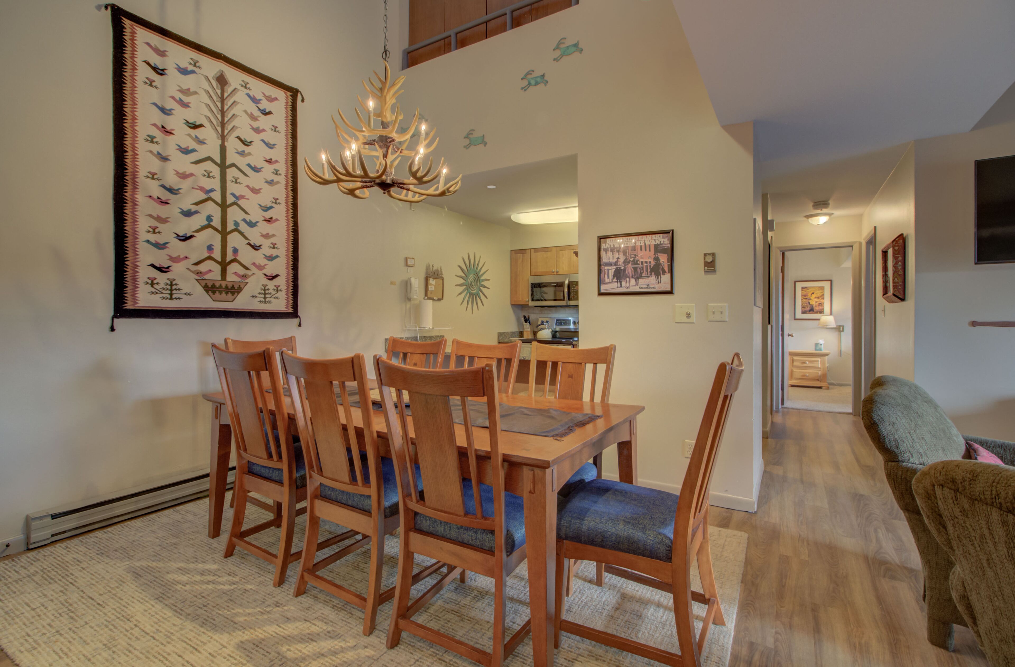 A dining area with a wooden table and chairs, a chandelier, and wall decorations including a bird mural and a sun design.