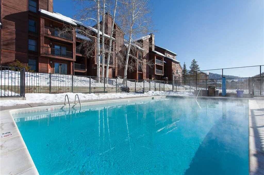 A clear blue pool adjacent to a building with multiple balconies and a snow-covered ground.