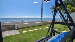 A view from a balcony overlooking a beach with a fountain, a concrete barrier, and a grassy area with a metal railing.