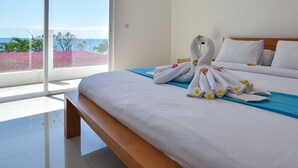 A hotel room with a large bed, a wooden bench, and a view of the ocean through large windows.