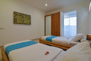 A hotel room with two beds, a large window with blinds, a wooden wardrobe, and a wall art piece.