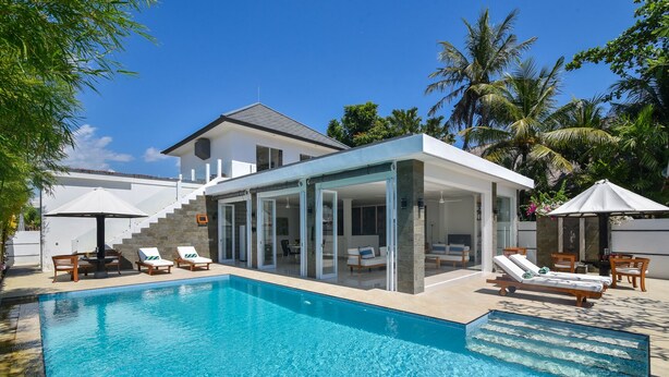 A modern house with a pool, featuring a glass-enclosed patio area with lounge chairs and a dining table.