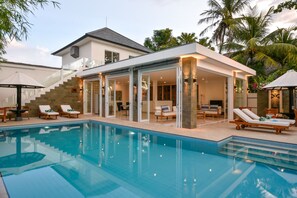 A modern poolside area with lounge chairs, a covered seating area, and a staircase leading to an upper level.